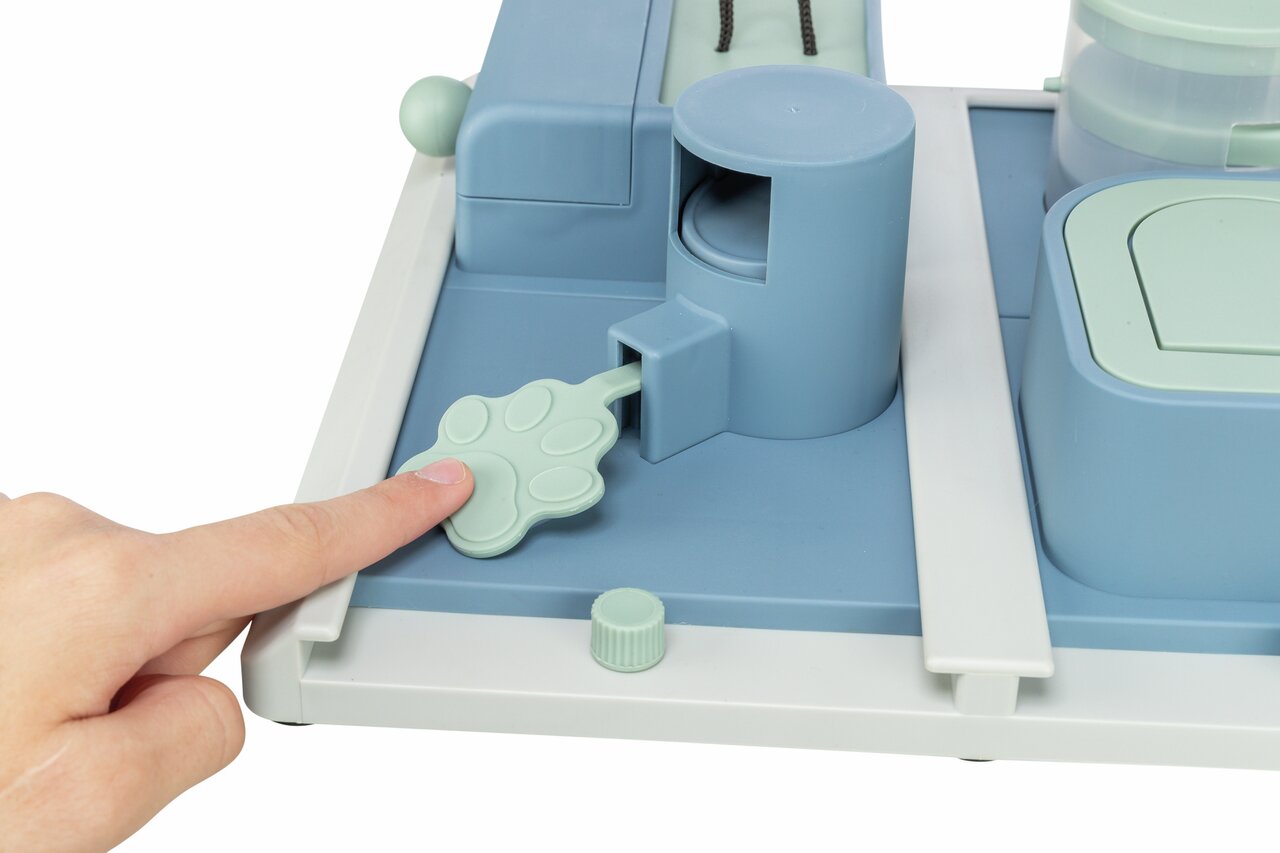 Finger zeigt auf ein hellgrünes Pfotenförmchen des TRIXIE Activity Strategiespiels für Hunde, ideal für mentale Auslastung.