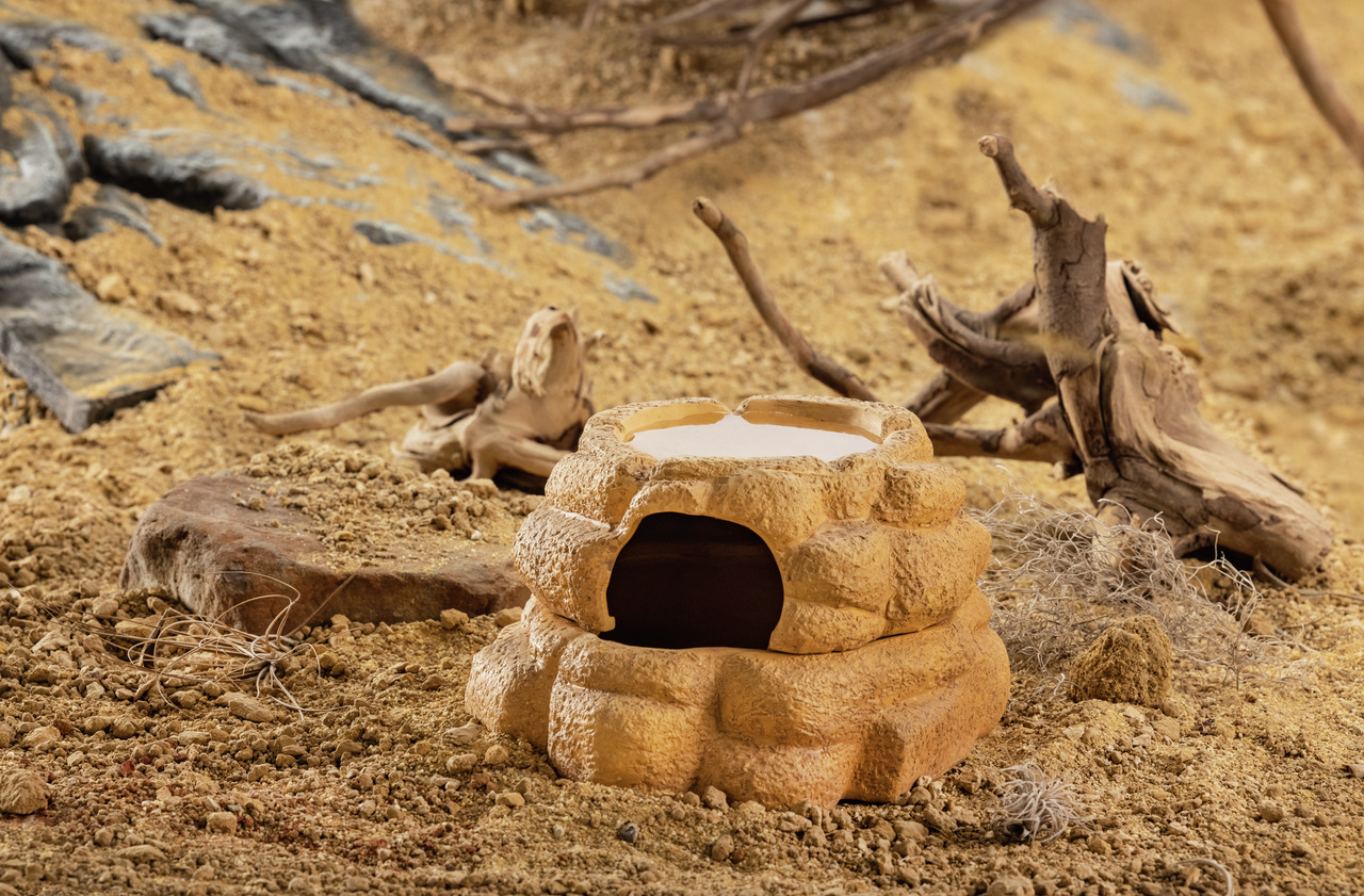 Das Bild zeigt das Exo Terra Reptilienversteck, ein natürlich aussehendes Versteck für Reptilien und Amphibien. Es ist aus robustem, gelblich-braunem Material gefertigt und erinnert an einen Felsen. Das Versteck bietet eine dunkle Höhle für Sicherheit und