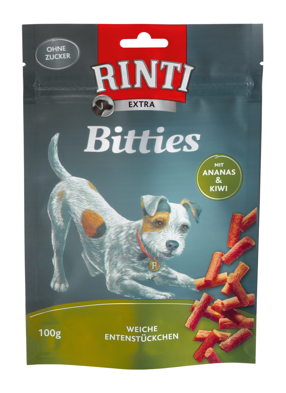 Das Bild zeigt eine Verpackung des Hundefutters „RINTI Extra Bitties“ in der Geschmacksrichtung Ente mit Ananas und Kiwi. Die Zielgruppe sind Hunde. Die Verpackung enthält 100 g weiche Entenstückchen, beworben als ohne Zucker. Im Vordergrund ist ein Hund 