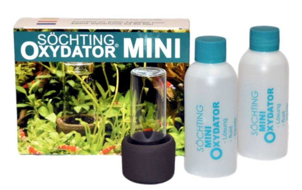 Das Bild zeigt den Söchting Oxydator Mini, ein Produkt für Aquarienbesitzer. Es besteht aus einem Glasbehälter mit schwarzem Sockel und zwei Flaschen Oxydator-Lösung. Im Hintergrund ist die Verpackung mit Pflanzen und Garnelen abgebildet. Der Oxydator sor