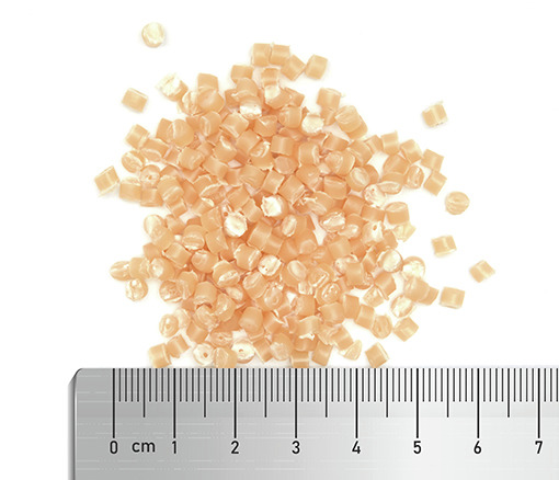 Orangefarbene Kunststoffgranulate (3-4 mm) auf weißer Fläche, mit Lineal zur Größenangabe (cm/mm).