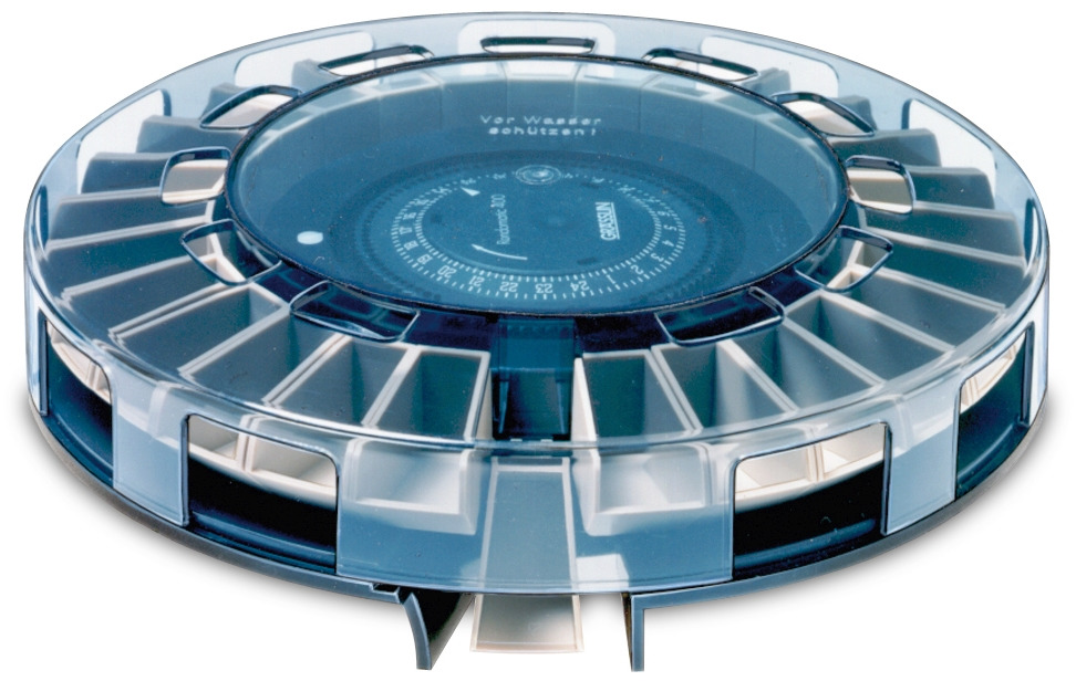 Das Bild zeigt einen runden Diakarussell-Magazin von der Marke Grässlin, Modell LKM 100. Es besteht aus transparentem Kunststoff mit einem blauen Deckel und bietet Platz für bis zu 100 Dias. Das Produkt ist ideal für die sichere Aufbewahrung und Präsentat