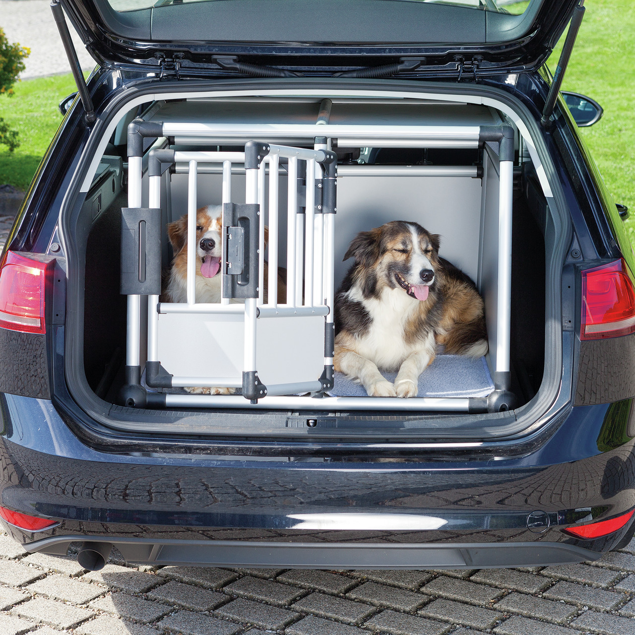 Das Bild zeigt einen geöffneten Kofferraum eines Autos, in dem zwei Hunde in einer stabilen Hundetransportbox der Marke TRIXIE untergebracht sind. Die Box ist aus Aluminium gefertigt und bietet Sicherheit und Komfort für Hunde während der Fahrt. Zielgrupp