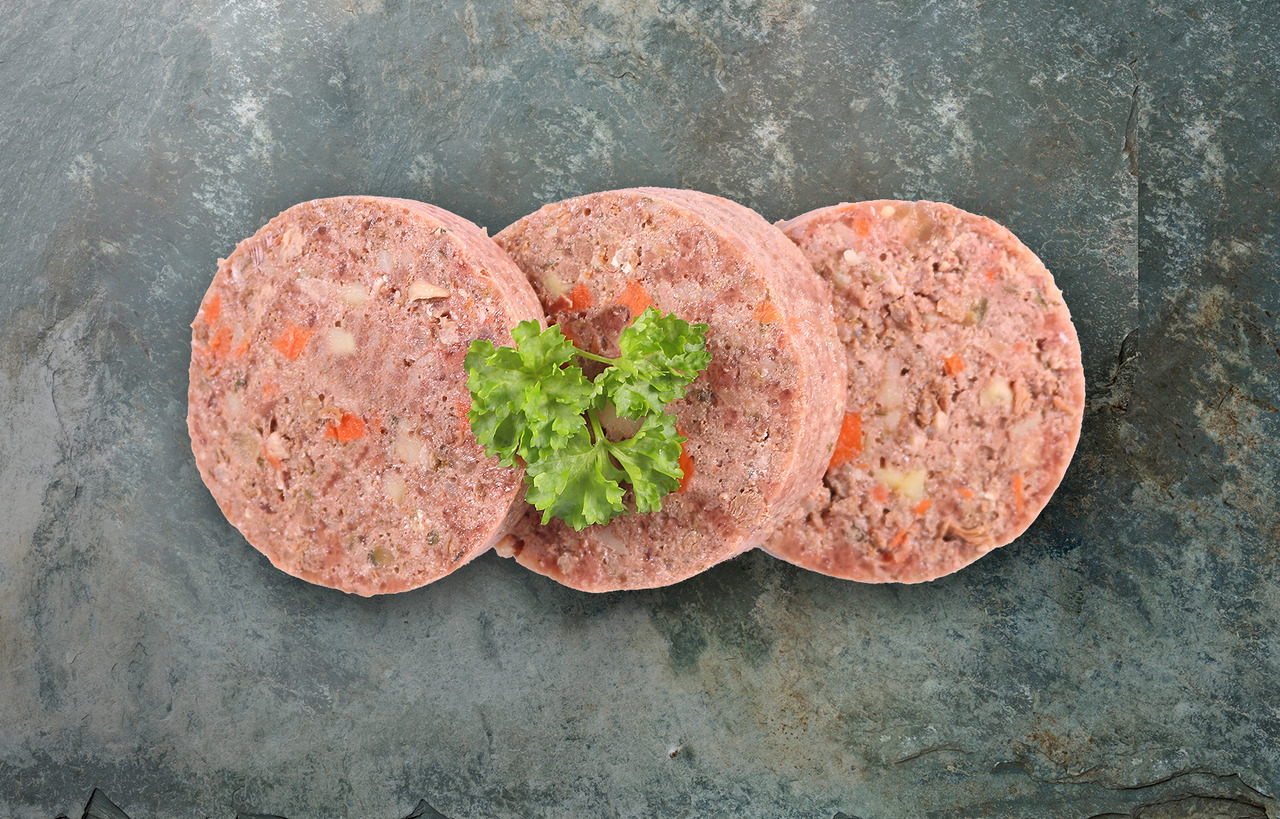 Auf dem Bild sind drei Scheiben des Hundefutters „Lakefields Nassfutter Rind mit Gemüse“ zu sehen, die auf einer dunklen Steinplatte arrangiert sind. Jede Scheibe zeigt eine Mischung aus Fleisch und sichtbaren Gemüsestücken wie Karotten und Kartoffeln. In