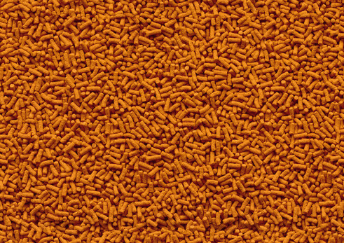 Das Bild zeigt eine Nahaufnahme von orangefarbenem Fischfutter in Pelletform. Es handelt sich um das Produkt „Tetra Pond Sticks“, ein Hauptfutter für Teichfische. Zielgruppe sind Teichfische, Geschmacksrichtung ist universell. Die Packungsmenge ist auf de