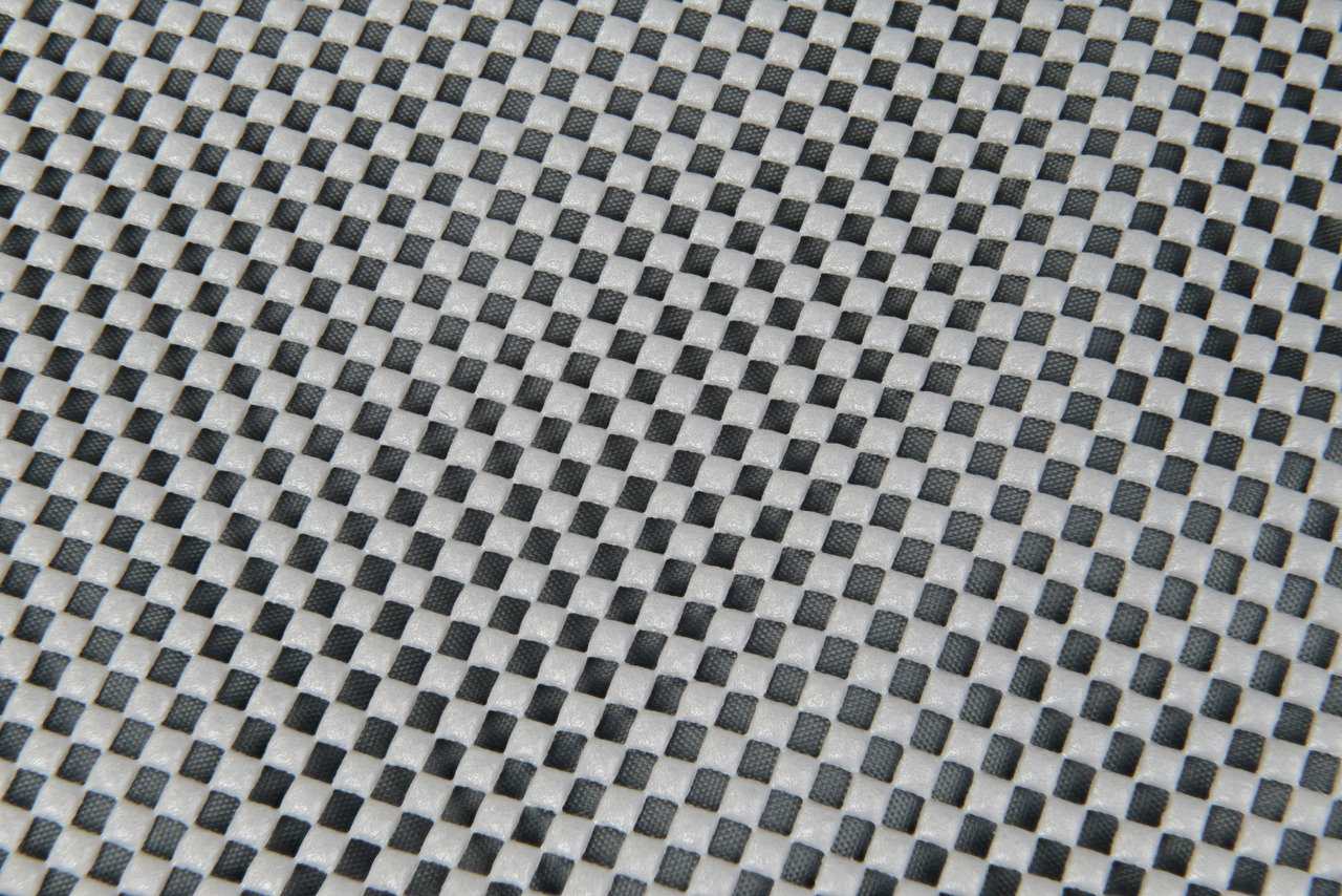 Das Bild zeigt eine Nahaufnahme einer strukturierten Oberfläche mit einem schwarz-weißen Schachbrettmuster. Es handelt sich um das Produkt AniOne Kühlmatte für Haustiere, geeignet für Hunde und Katzen. Die Matte bietet eine kühlende Wirkung ohne Strom ode