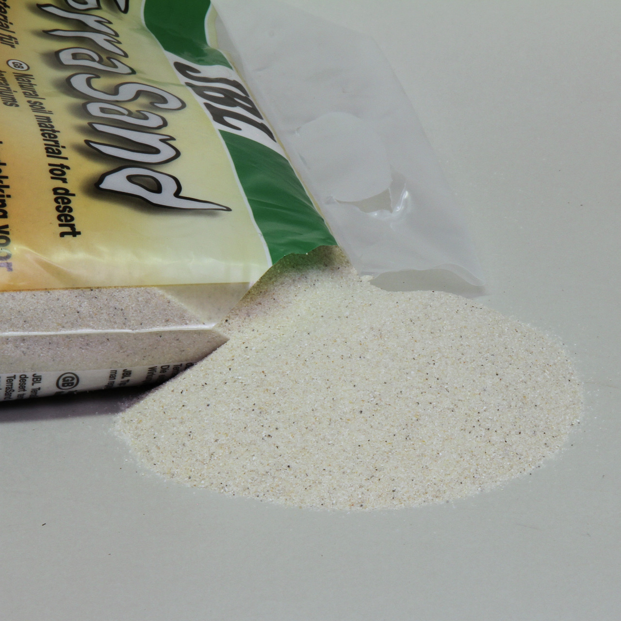 Das Bild zeigt eine geöffnete Verpackung des Produkts JBL TerraSand, einem natürlichen Wüstensand für Terrarien. Der Sand ist beige und fein, ideal für Wüstentiere wie Reptilien. Die Zielgruppe sind Terrarienbesitzer. Die Verpackung enthält 5 kg Sand, wie