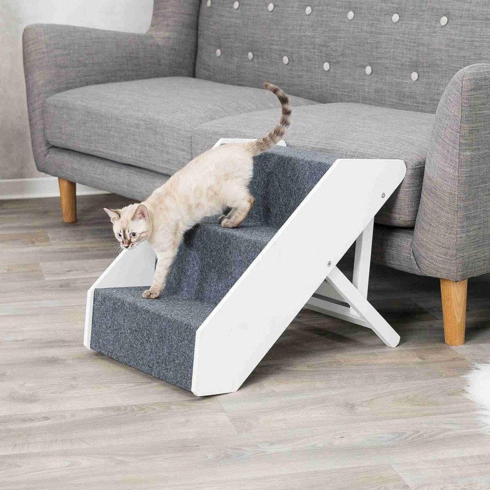 Das Bild zeigt eine TRIXIE Haustiertreppe, geeignet für Katzen und kleine Hunde, vor einem grauen Sofa. Die weiße Treppe mit grauem Teppichbelag erleichtert den Zugang zu erhöhten Flächen und schützt Gelenke. Ideal für ältere oder verletzte Tiere. Maße un