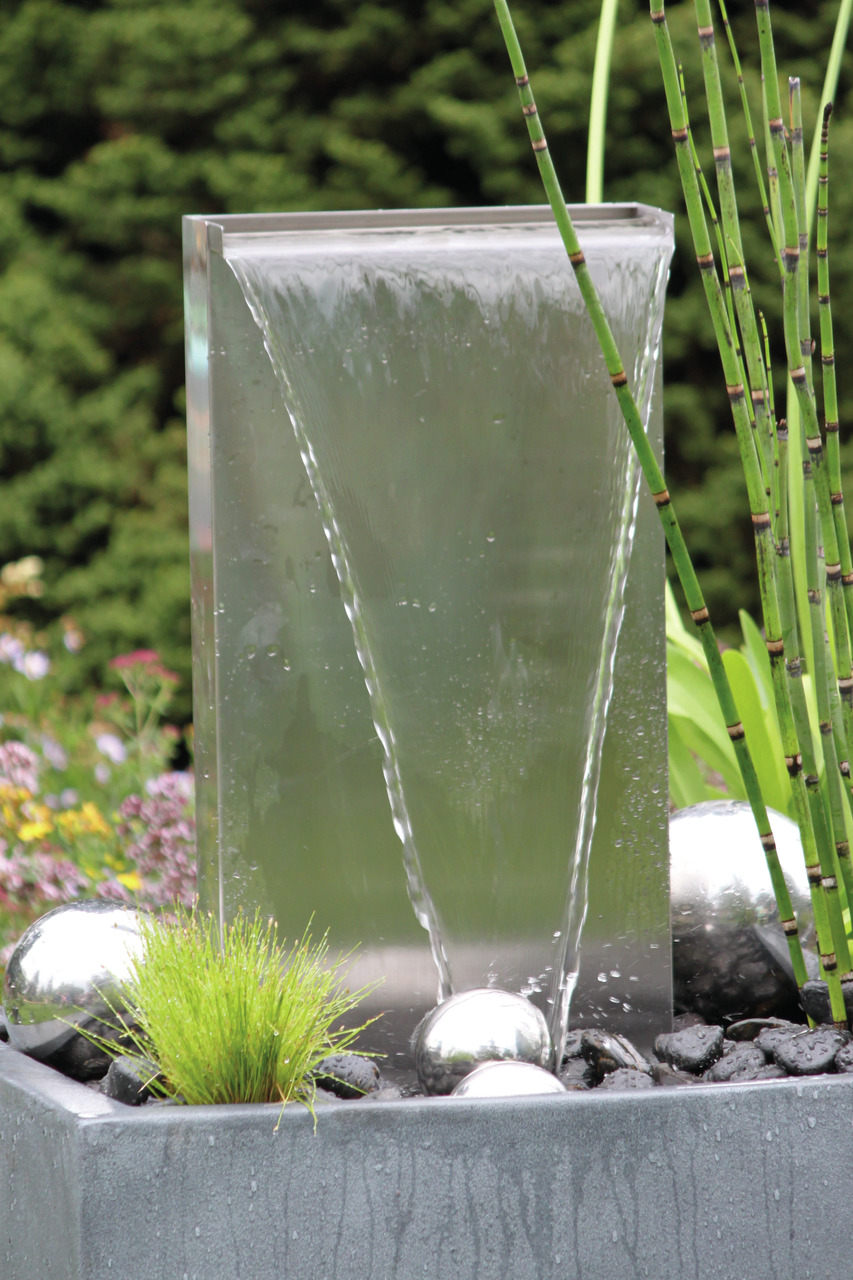 Oase Edelstahl-Wasserfall, sanfter Fluss über glatte Metallfläche, ideal für Gartenliebhaber, dekorativ mit Pflanzen & Steinen.