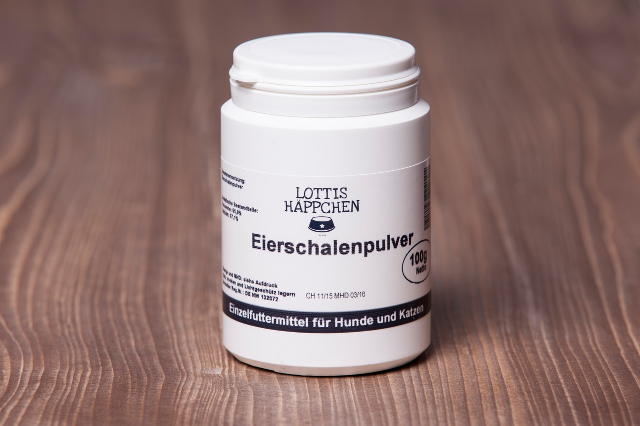 Das Bild zeigt eine weiße Kunststoffdose des Produkts „Lottis Häppchen Eierschalenpulver“ mit einem Inhalt von 100 g. Es handelt sich um ein Einzelfuttermittel für Hunde und Katzen. Die Verpackung steht auf einer Holzoberfläche, und die Beschriftung hebt 
