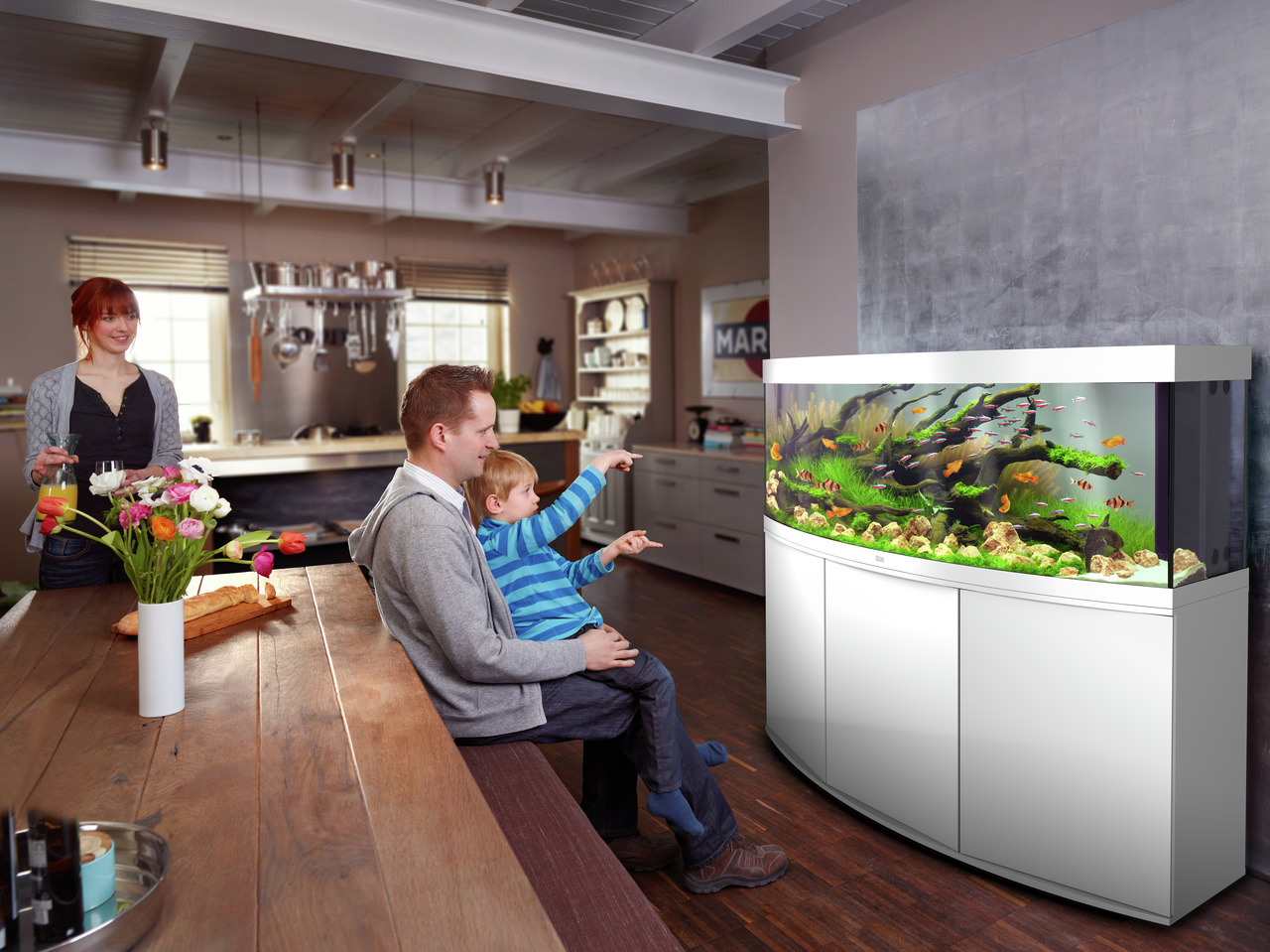 Das Bild zeigt ein modernes Wohnzimmer mit einem großen, weißen JUWEL-Aquarium, das mit bunten Fischen, grünen Wasserpflanzen und dekorativen Steinen ausgestattet ist. Das Aquarium ist ideal für Aquaristik-Enthusiasten und bietet eine stilvolle Ergänzung 