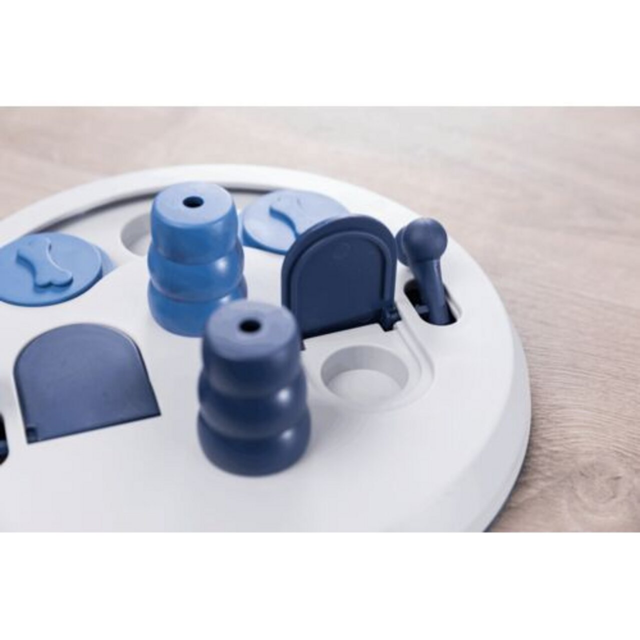 Das Bild zeigt das TRIXIE Dog Activity Flip Board, ein interaktives Intelligenzspielzeug für Hunde. Es ist speziell für Hunde aller Größen und Altersgruppen konzipiert, um ihre geistige Auslastung zu fördern. Das Spielzeug besteht aus einem weißen runden 