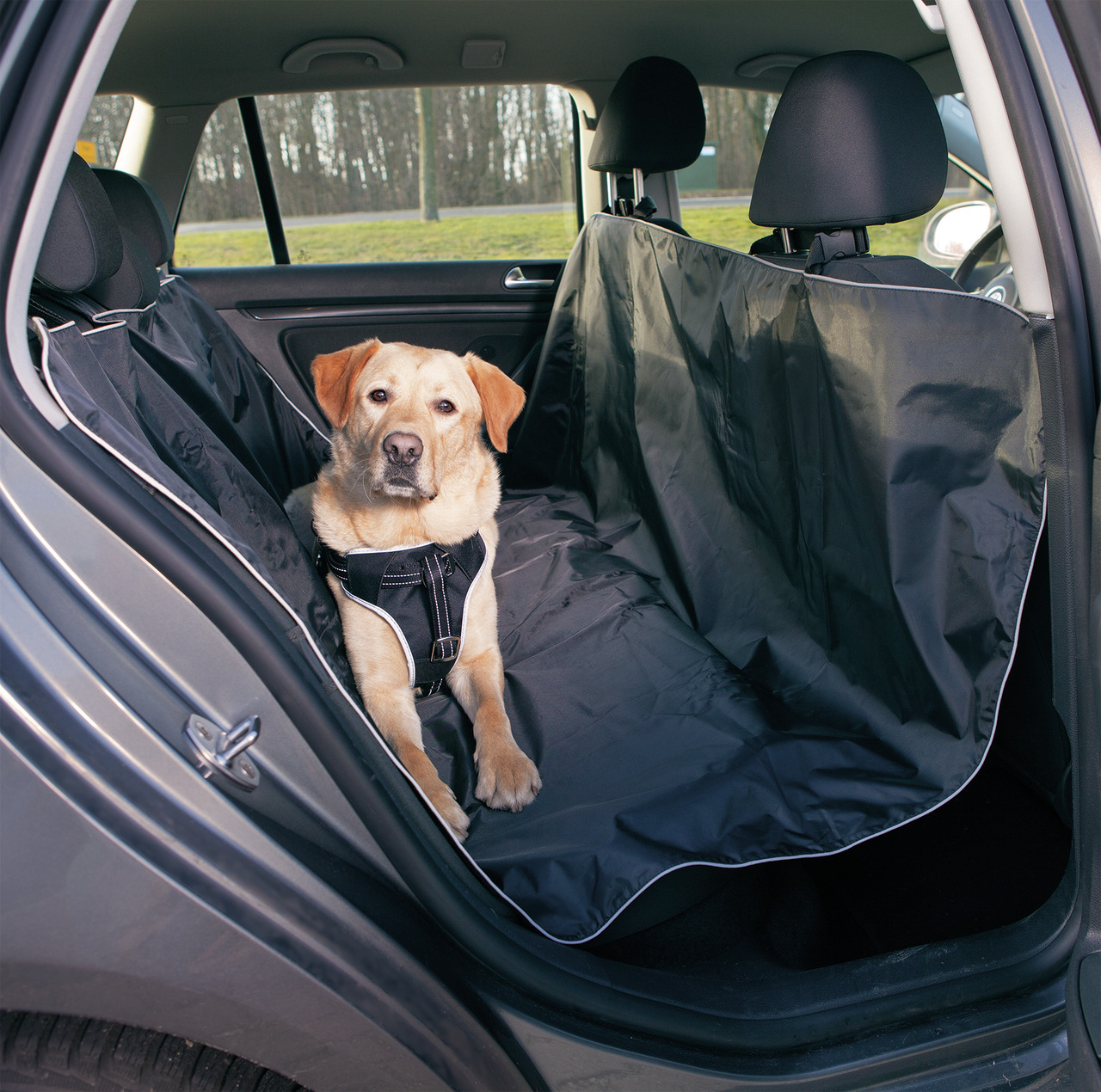 Auf dem Bild ist eine schwarze Autoschondecke der Marke TRIXIE zu sehen, die speziell für Hunde entwickelt wurde. Sie schützt die Rückbank vor Schmutz, Haaren und Feuchtigkeit. Ein Hund sitzt auf der Decke, die sicher befestigt ist. Ideal für Tierhalter, 