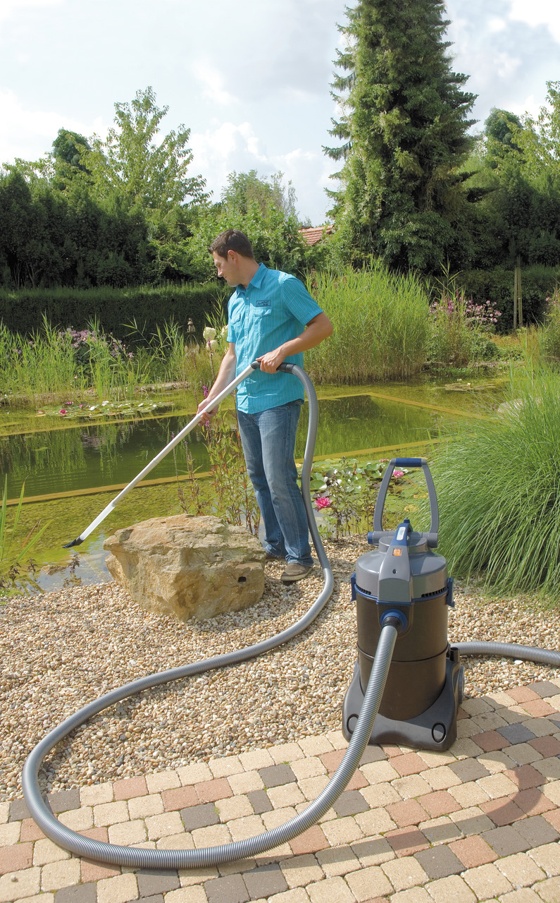 Auf dem Bild ist ein Oase Pondovac Teichsauger zu sehen, der für die Reinigung von Gartenteichen entwickelt wurde. Ein Mann verwendet den Sauger, um Algen und Schmutz vom Teichboden zu entfernen. Der Sauger ist mit einem langen Schlauch und einem stabilen