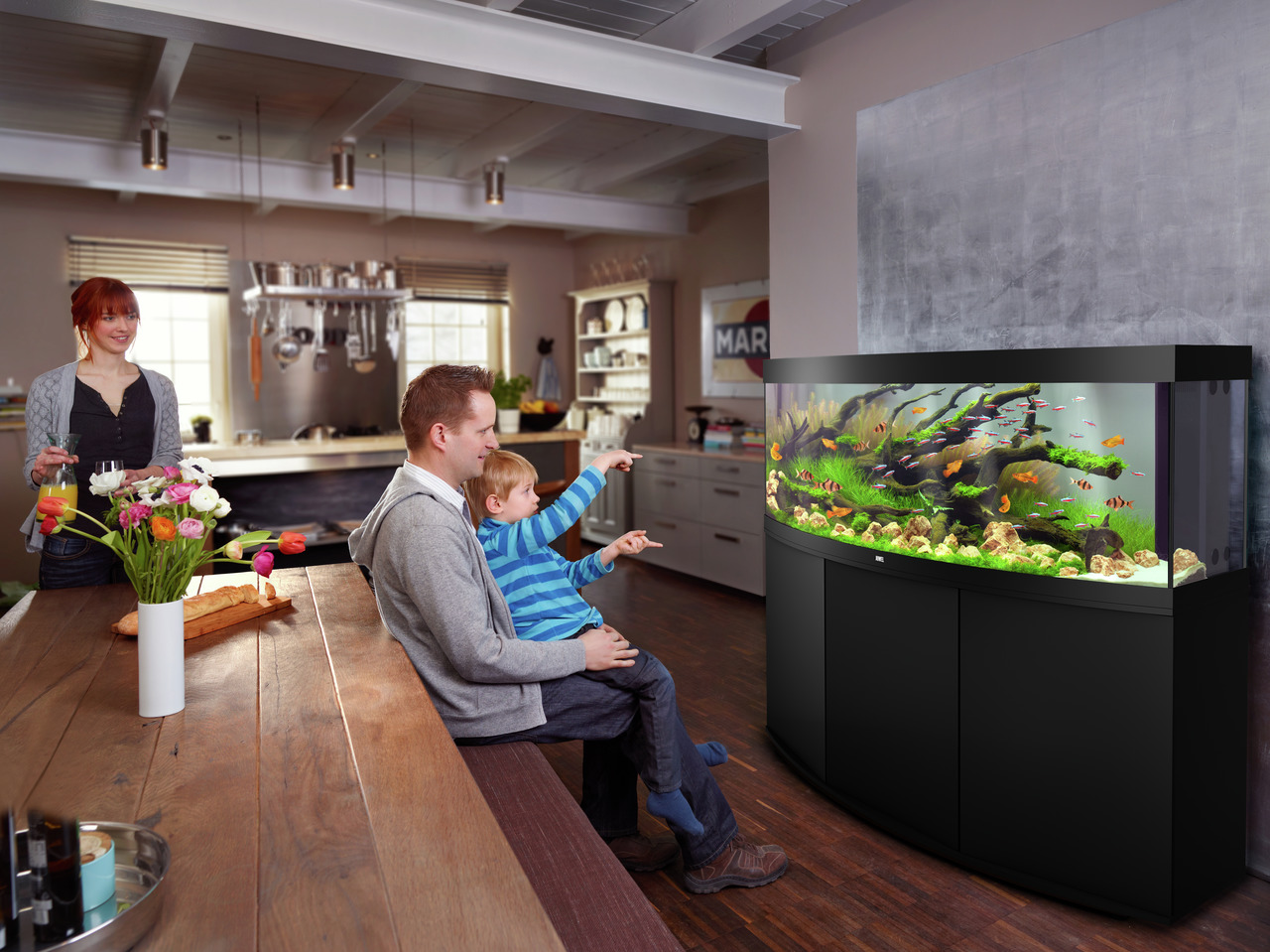 Ein modernes Wohnzimmer mit einem großen JUWEL-Aquarium, Modell Vision 450, im Vordergrund. Das Aquarium ist für Aquaristik-Enthusiasten geeignet und zeigt eine lebendige Unterwasserwelt mit Fischen, Pflanzen und Dekoration. Es hat ein elegantes, schwarze