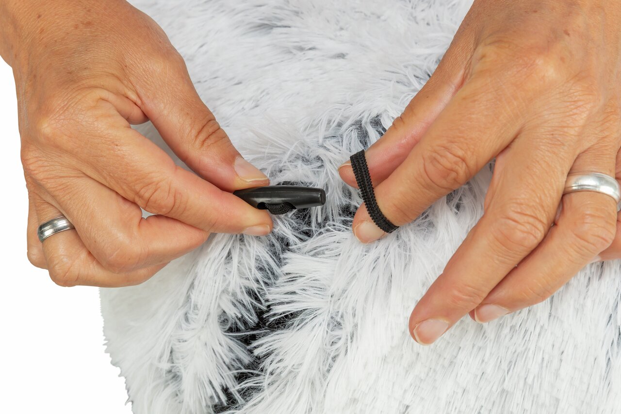 Hände justieren einen schwarzen Gummizug mit Verschluss an einem weißen, flauschigen Material, Nahaufnahme.