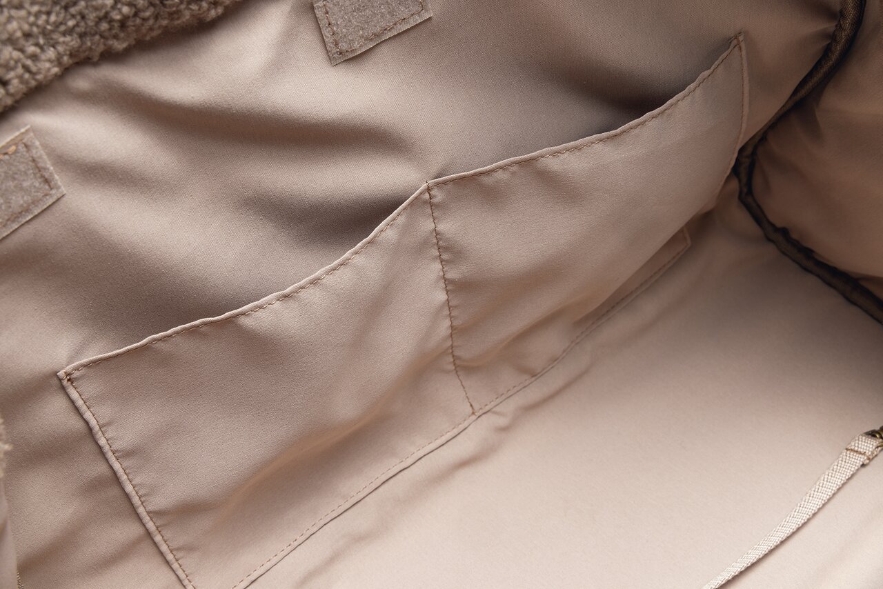 Innenansicht einer beigen Tragetasche von Designed by Lotte mit weichem Stoff und mehreren Taschen für Zubehör.
