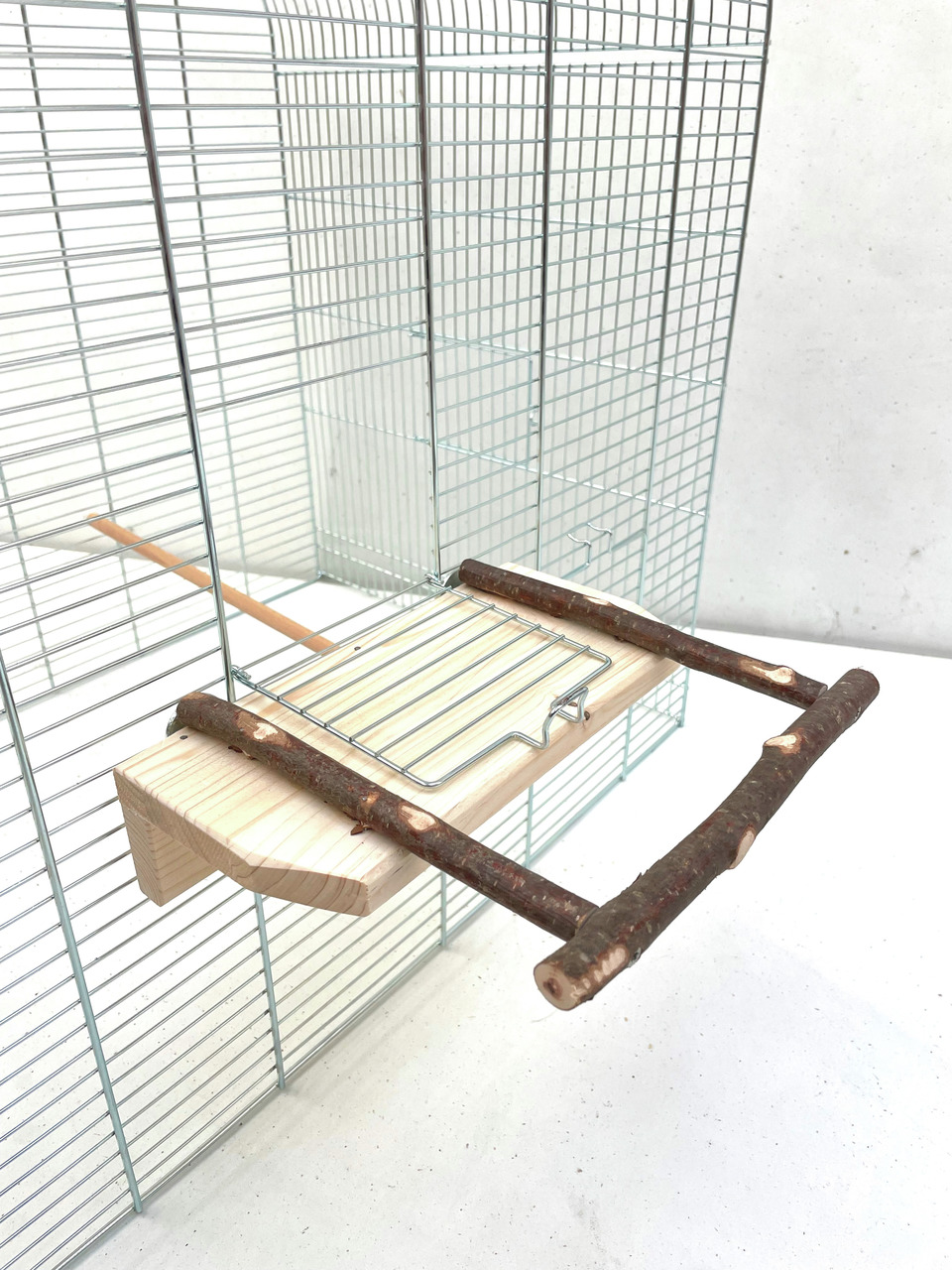 Das Bild zeigt eine hochwertige Vogel-Sitzstange der Marke Ollesch, geeignet für Vögel wie Wellensittiche und Kanarienvögel. Die Sitzstange besteht aus natürlichem Holz und ist an einem Vogelkäfig befestigt. Sie bietet eine stabile Sitzfläche und fördert 