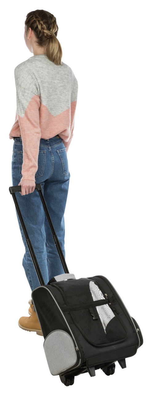 Das Bild zeigt eine Frau von hinten, die einen schwarzen TRIXIE Trolley für Haustiere zieht. Der Trolley ist mit Netzfenstern für Belüftung ausgestattet und hat seitliche Taschen. Zielgruppe sind Haustierbesitzer, die ihre Tiere bequem transportieren möch