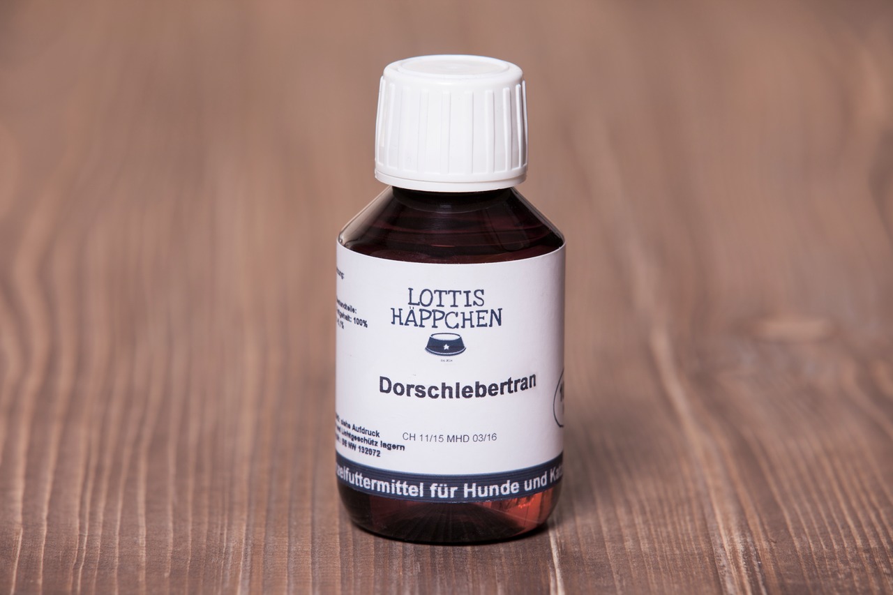 Das Bild zeigt eine braune Glasflasche mit weißem Schraubverschluss der Marke "Lottis Häppchen". Auf dem Etikett steht "Dorschlebertran", ein Ergänzungsfuttermittel für Hunde und Katzen. Die Flasche enthält 100 ml und ist auf einer Holzoberfläche platzier