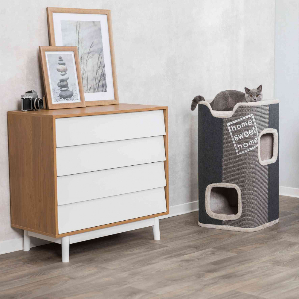 Das Bild zeigt einen modernen Kratzbaum der Marke TRIXIE, Modell „Home Sweet Home“, geeignet für Katzen. Der Kratzbaum ist grau mit beigen Details und bietet mehrere Öffnungen sowie eine Liegefläche. Eine graue Katze liegt entspannt oben. Im Hintergrund s