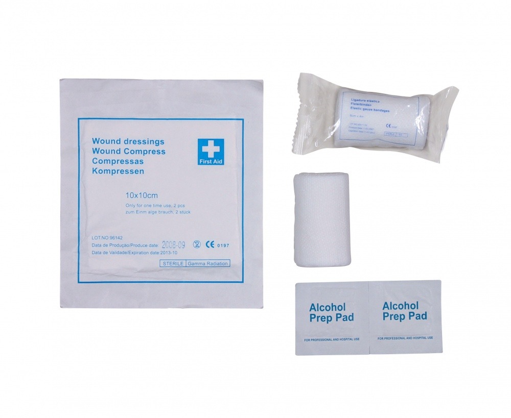 Das Bild zeigt ein Erste-Hilfe-Set mit mehreren Komponenten, darunter sterile Wundkompressen (10x10 cm, 2 Stück), elastische Mullbinden (8 cm x 4 m) und zwei Alkoholtupfer zur Desinfektion. Die Verpackung der Kompressen ist mit blauer Schrift beschriftet 