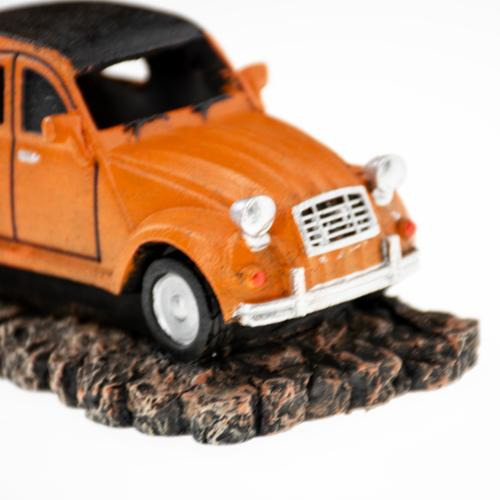 Ein orangefarbenes Modellauto im Retro-Stil, das auf einer felsigen Basis steht. Es handelt sich um ein Dekorationsobjekt der Marke AQUA DELLA, geeignet für Aquarien. Das Auto hat detaillierte Scheinwerfer, einen schwarzen Dachbereich und eine realistisch