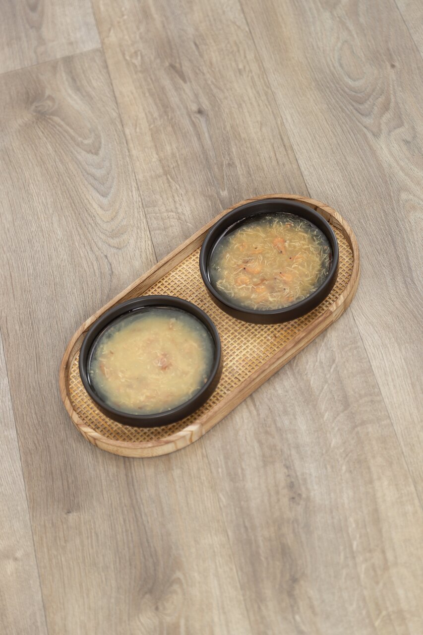 Zwei Schalen TRIXIE Katzensuppe mit Huhn und Gemüse auf einem Bambustablett, ideal für Katzen, 50 g pro Portion.