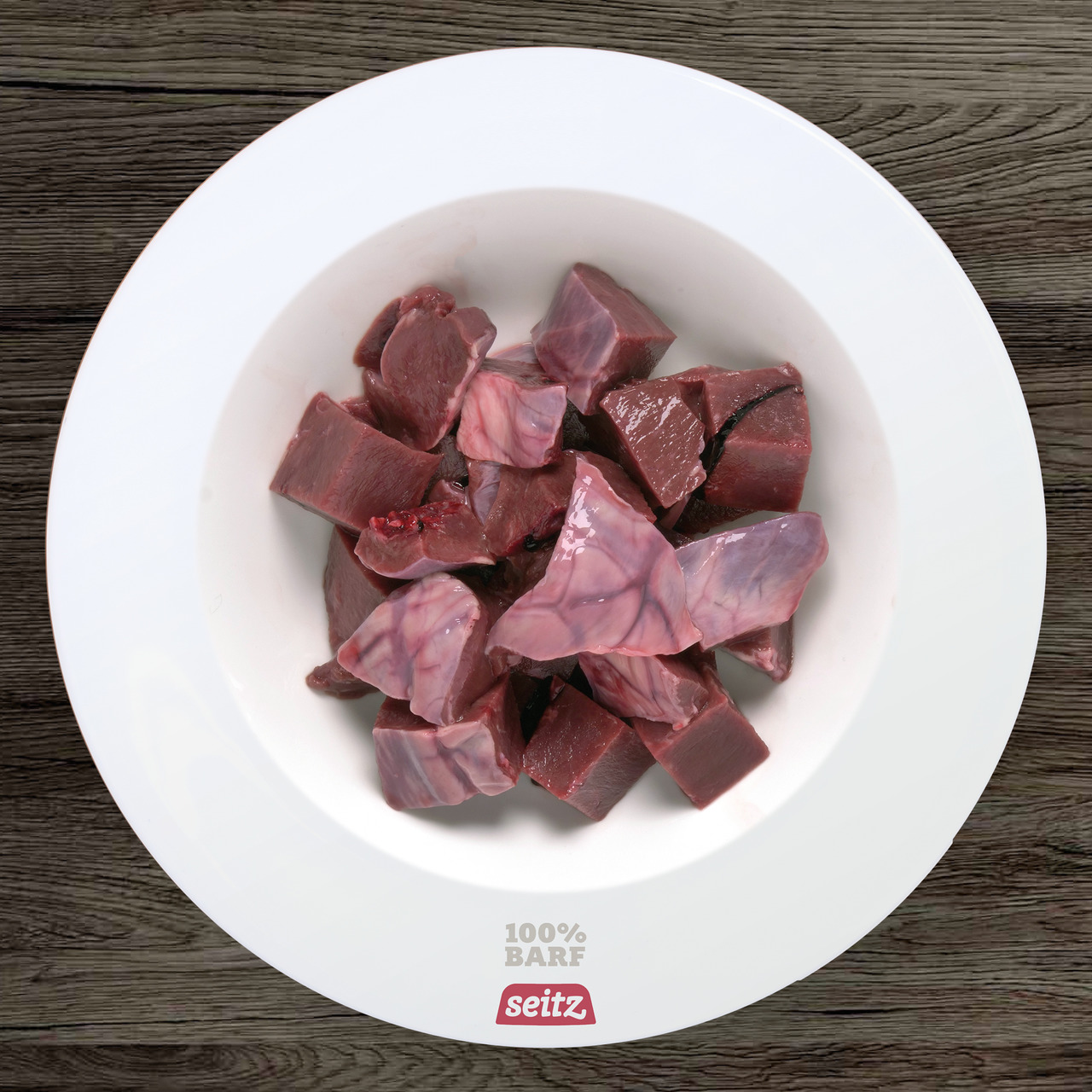 Das Bild zeigt eine weiße Schale, die mit rohen Fleischstücken gefüllt ist. Es handelt sich um das Produkt "Seitz 100% BARF Rindermix", ein hochwertiges BARF-Futter für Hunde. Zielgruppe sind Hundehalter, die auf natürliche Ernährung setzen. Die Fleischst