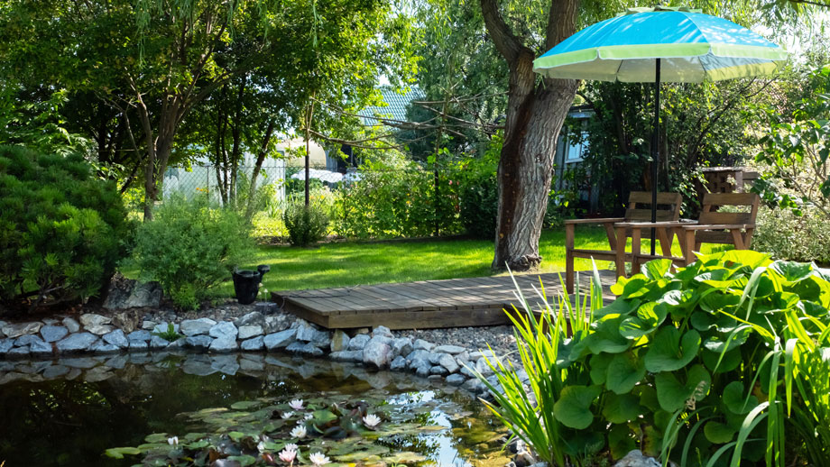 Gemütliche Gartenecke mit Teich, Sitzplatz und Sonnenschirm zum Entspannen.