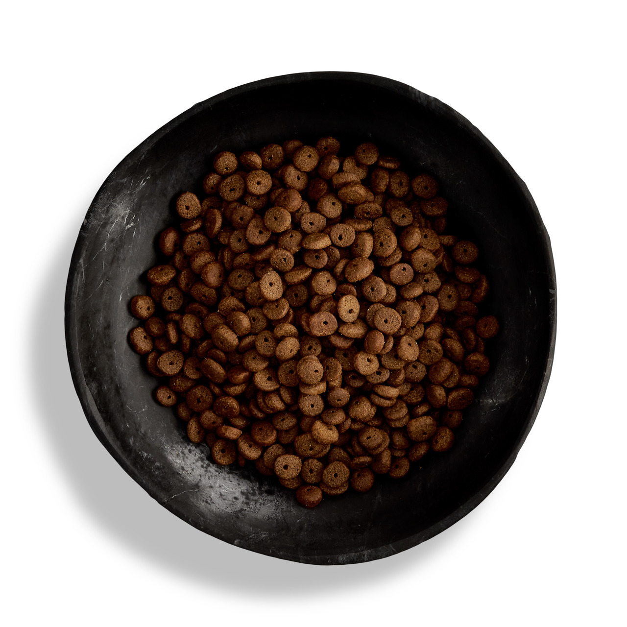 Das Bild zeigt eine schwarze Schale, die mit braunen, runden Trockenfutterstücken gefüllt ist. Es handelt sich um das Produkt "Canagan Free-Run Chicken" für Hunde. Dieses getreidefreie Premium-Hundefutter ist für alle Altersgruppen geeignet und hat Huhn a