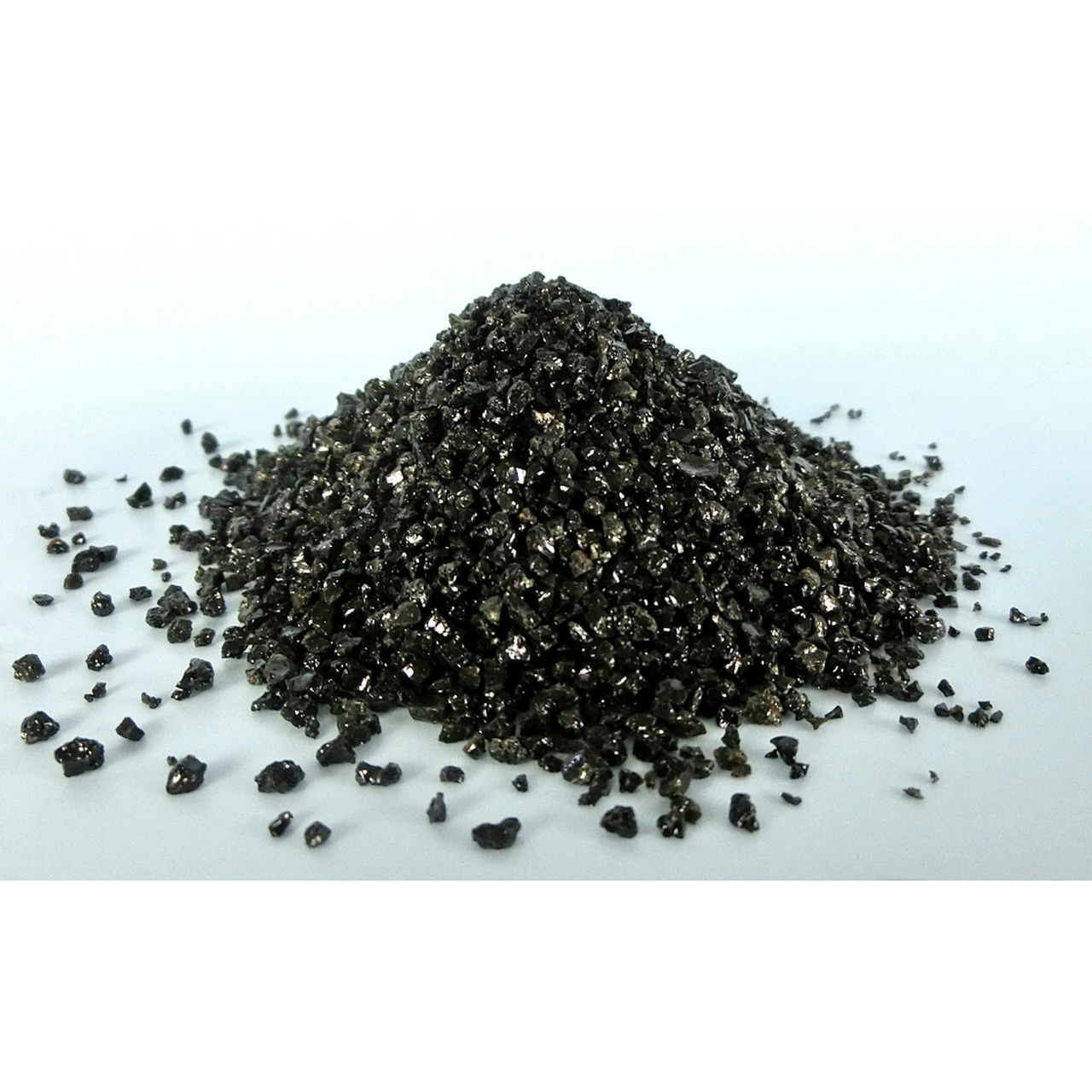 Schwarzes, glänzendes Granulat auf weißer Fläche, körnig, lichtreflektierend, evtl. kristallin, mögliches Schleifmittel o.ä. Produkt.