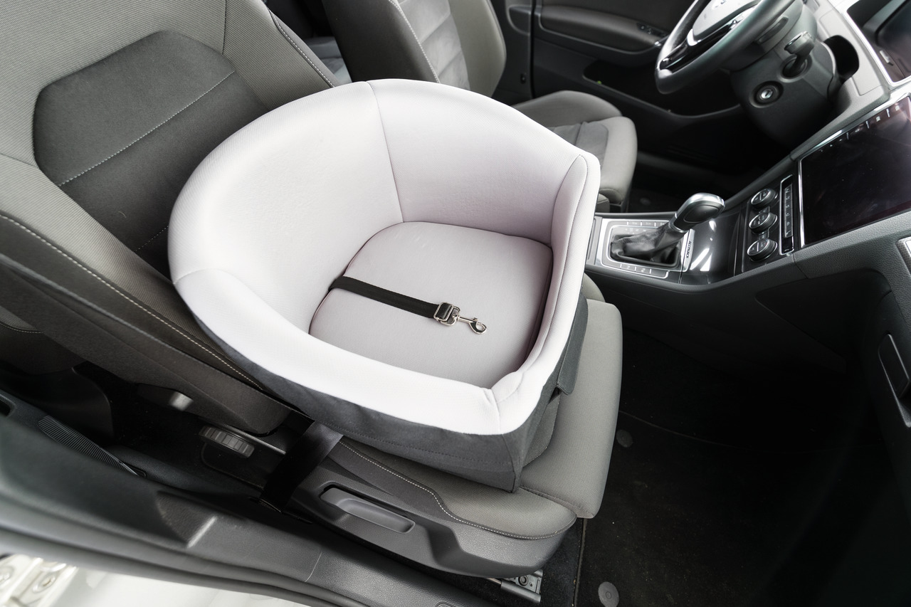 Das Bild zeigt den TRIXIE Autositz für Hunde, ein hochwertiges Produkt für den sicheren Transport kleiner Hunde im Auto. Der Sitz ist in hellgrauer Farbe gehalten, mit gepolsterten Seitenwänden und einem integrierten Sicherheitsgurt. Er ist speziell für k