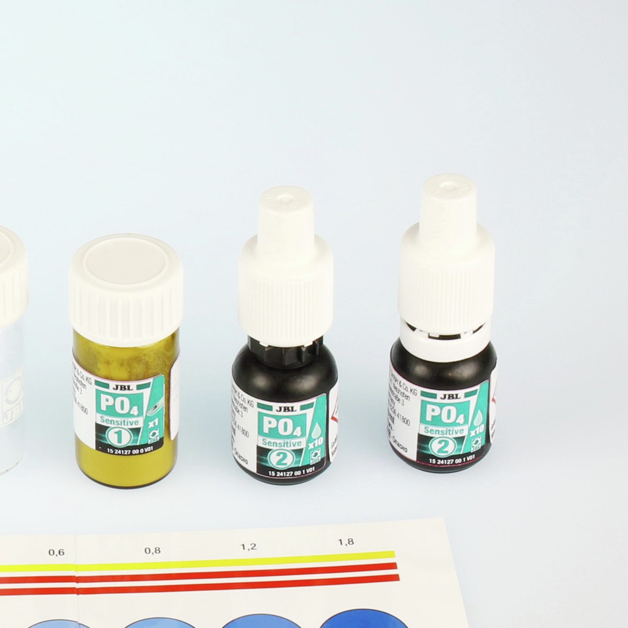 Das Bild zeigt das JBL PO4 Sensitive Wassertest-Set, ein Produkt für Aquaristik-Enthusiasten. Es besteht aus drei Fläschchen mit Reagenzien, die zur präzisen Messung des Phosphatgehalts im Wasser dienen. Im Vordergrund ist eine Farbskala zur Auswertung de