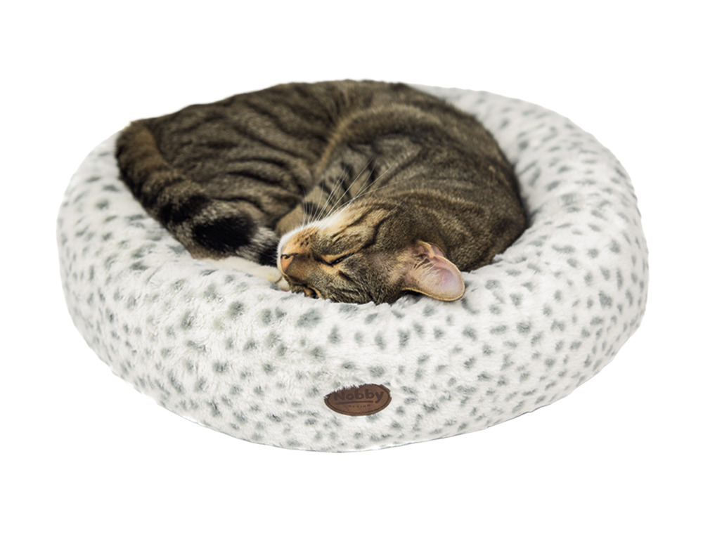 Ein getigerter Hauskater schläft gemütlich in einem runden, flauschigen Katzenbett der Marke Nobby. Das Bett ist weiß mit grauen Punkten und hat ein weiches, gepolstertes Design. Es richtet sich an Katzenbesitzer, die ihren Tieren Komfort bieten möchten. 