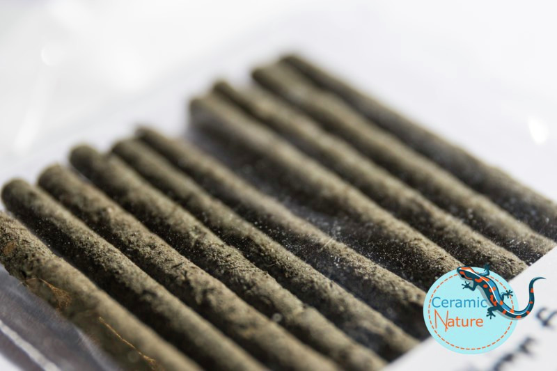 Das Bild zeigt eine Nahaufnahme von dunklen, länglichen Sticks, die in einer transparenten Verpackung angeordnet sind. Es handelt sich um das Produkt „CeramicNature Shrimp Sticks“, ein hochwertiges Futter für Garnelen. Die Sticks sind reich an Nährstoffen