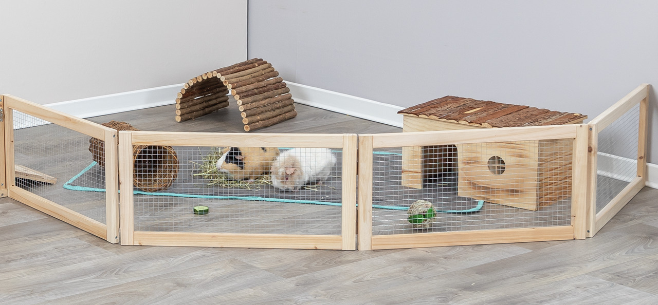 Auf dem Bild ist ein Freigehege der Marke TRIXIE für Kleintiere wie Meerschweinchen oder Kaninchen zu sehen. Das Gehege besteht aus einem stabilen Holzrahmen mit Drahtgitter und enthält Zubehör wie einen Tunnel, ein Häuschen und Spielzeug. Es bietet eine 