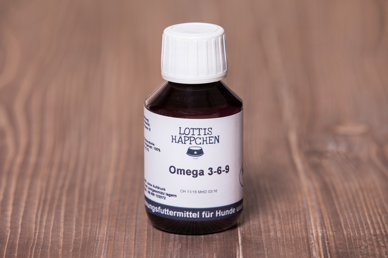 Das Bild zeigt eine braune Glasflasche mit weißem Schraubverschluss der Marke "Lottis Häppchen". Das Produkt ist ein Ergänzungsfuttermittel für Hunde mit der Bezeichnung "Omega 3-6-9". Die Flasche enthält 100 ml und ist auf einem Holztisch platziert. Die 
