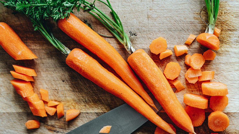 Teilweise geschnittene, teilweise ganze Möhren mit Möhrengrün auf Holzbrett