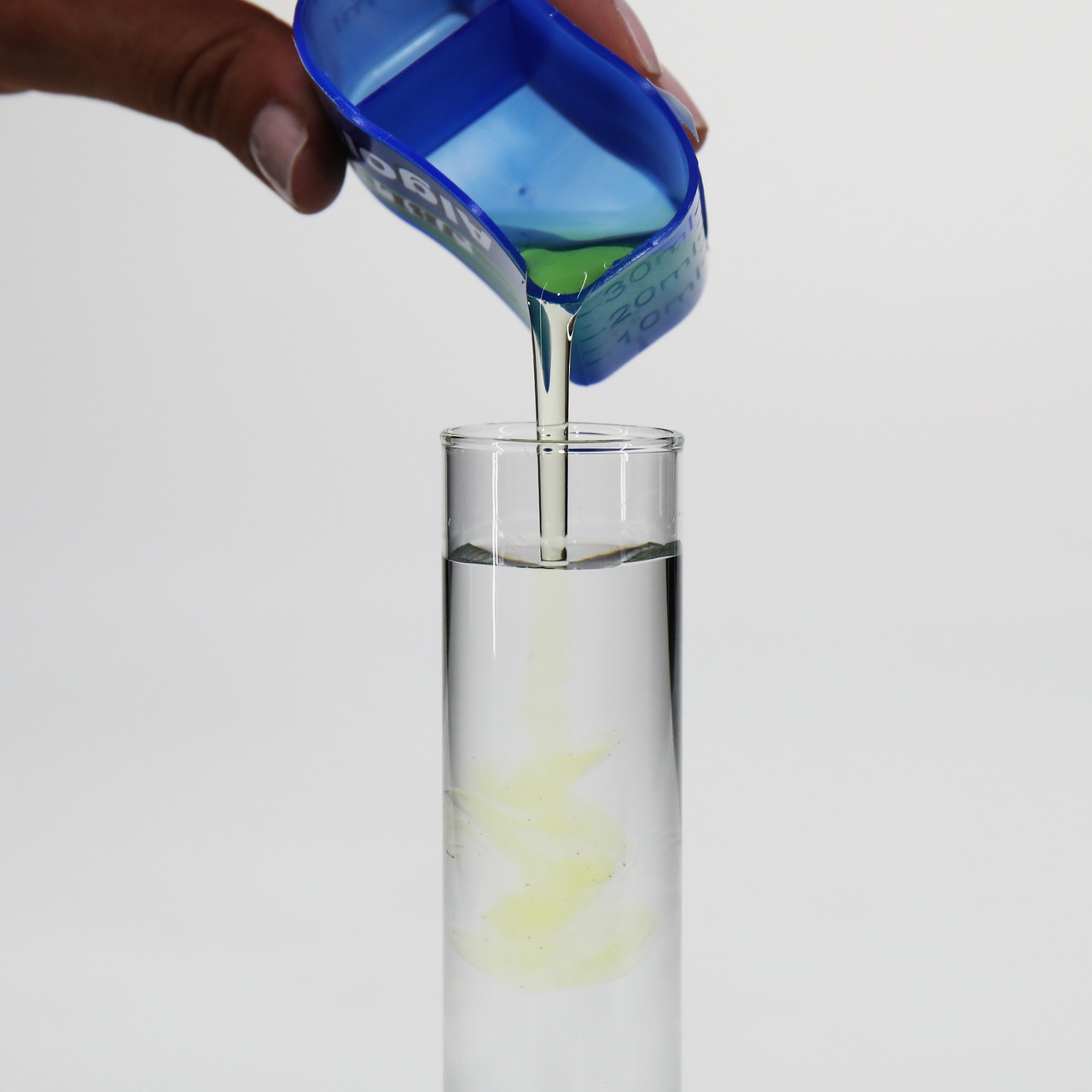 Das Bild zeigt eine Hand, die eine blaue Dosierhilfe hält, aus der eine klare Flüssigkeit in ein Reagenzglas gegossen wird. Es handelt sich um das Produkt JBL Denitrol, ein Wasseraufbereiter für Aquarien. Zielgruppe sind Aquarienbesitzer. Die Menge in der