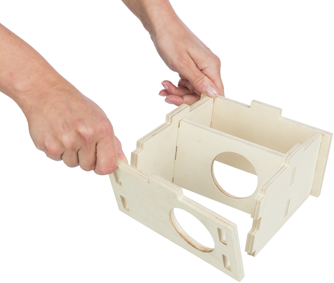 Auf dem Bild sind zwei Hände zu sehen, die ein Holzhaus von TRIXIE zusammenbauen. Das Produkt ist ein Nagerhaus für Kleintiere wie Hamster oder Mäuse. Es besteht aus naturbelassenem Holz und hat runde Eingänge. Zielgruppe sind Kleintierhalter. Das Haus is