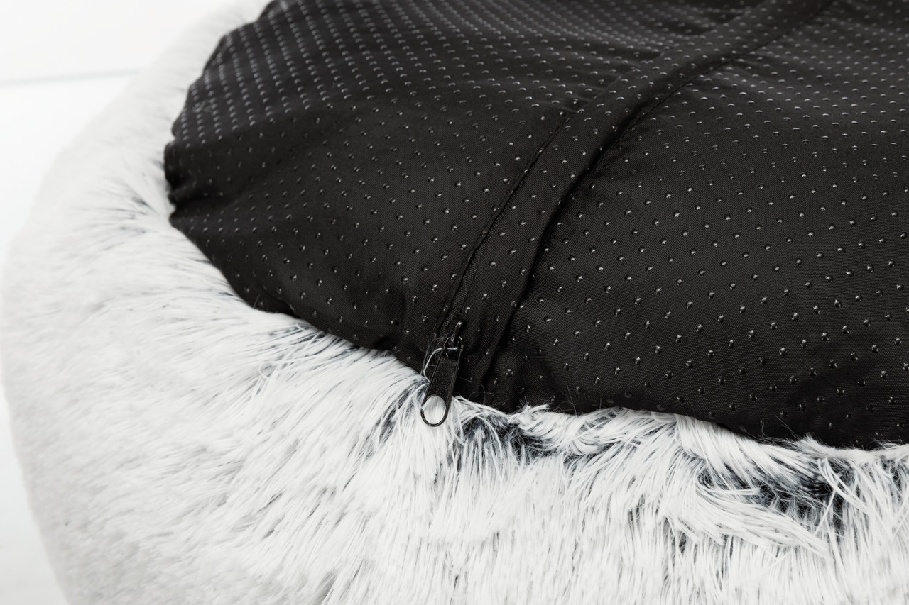 Das Bild zeigt das TRIXIE Kuschelbett für Haustiere, geeignet für Hunde und Katzen. Es hat eine weiche, weiße Plüschoberfläche und eine rutschfeste, schwarze Unterseite mit kleinen Noppen. Der Reißverschluss ermöglicht das Entfernen des Bezugs zur Reinigu