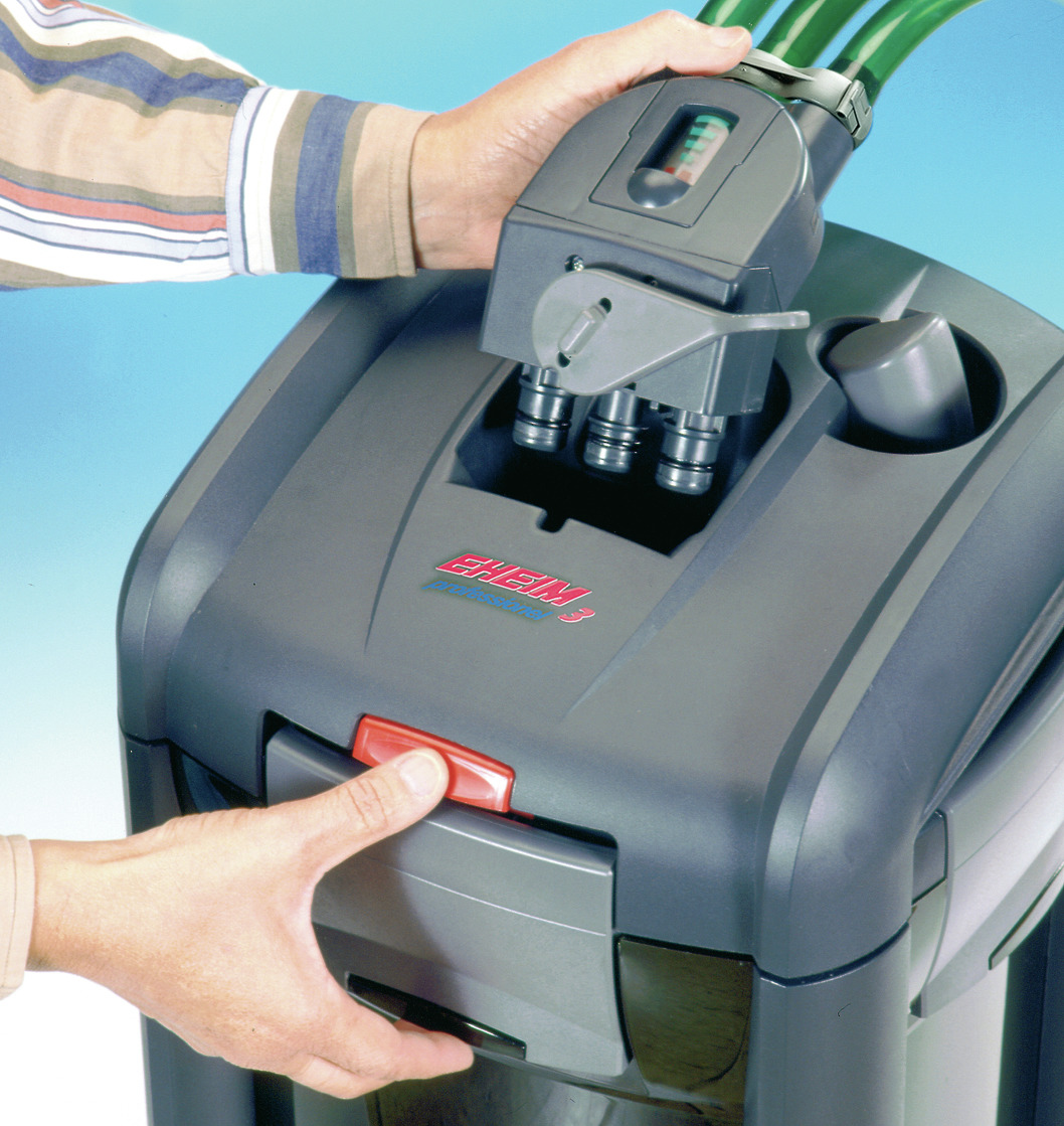 Das Bild zeigt den EHEIM professionel 3 Außenfilter, ein hochwertiges Produkt für die Aquaristik. Es richtet sich an Aquarienbesitzer und dient der effizienten Wasserfilterung. Zu sehen ist eine Nahaufnahme des Filters mit einer Hand, die den roten Versch