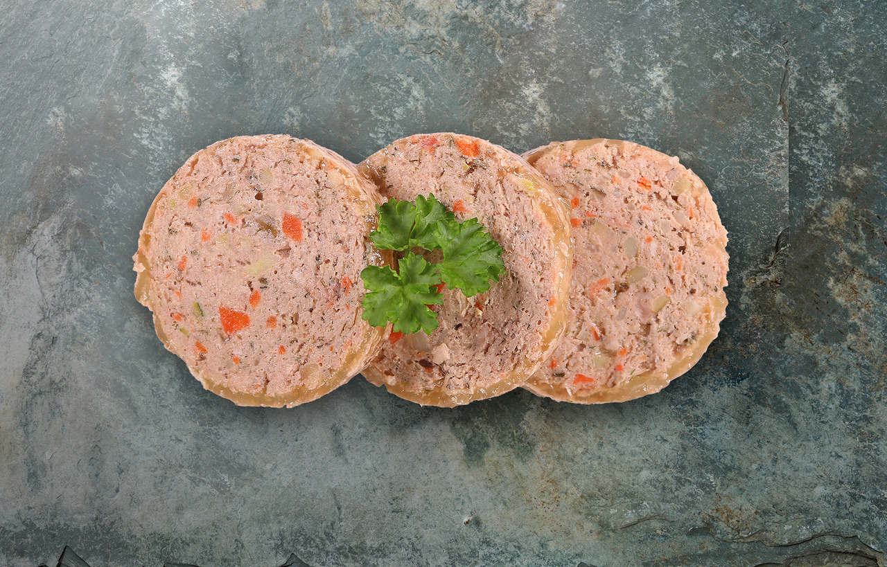 Das Bild zeigt drei Scheiben des Hundefutters „Lakefields Nassfutter Rind mit Gemüse“ auf einer dunklen Steinplatte. Die Scheiben bestehen aus einer Mischung aus Rindfleisch, Karotten und weiteren Gemüsestücken, dekoriert mit einem frischen Petersilienzwe