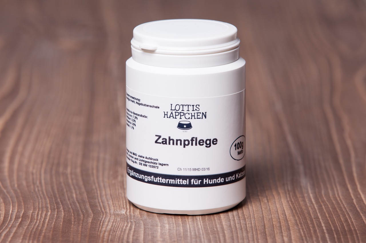 Das Bild zeigt ein weißes Kunststoffgefäß mit Schraubdeckel der Marke "Lottis Häppchen". Das Produkt trägt den Namen "Zahnpflege" und ist ein Ergänzungsfuttermittel für Hunde und Katzen. Die Verpackung enthält 100 g. Es steht auf einer Holzoberfläche, und