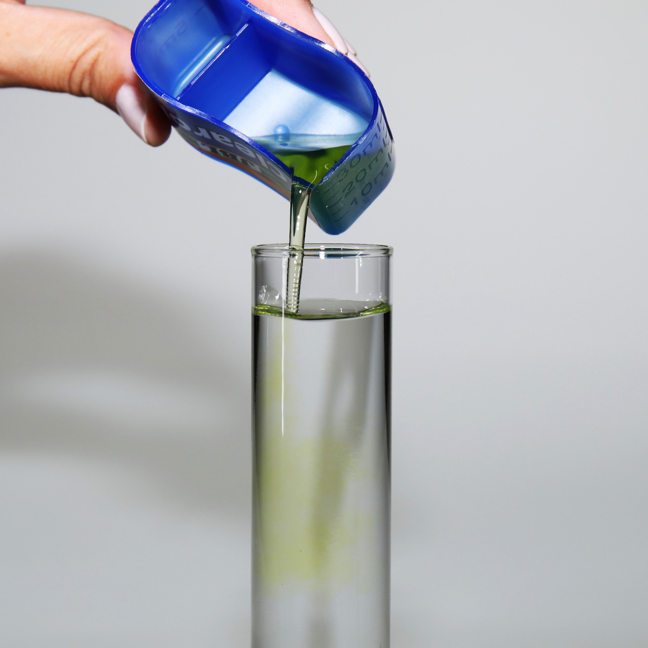 Das Bild zeigt eine Hand, die eine blaue Dosierhilfe hält, aus der eine grünliche Flüssigkeit in ein hohes, schmales Glasgefäß gegossen wird. Es handelt sich um das Produkt JBL Denitrol, ein Wasseraufbereiter für Aquarien. Zielgruppe sind Aquarienbesitzer