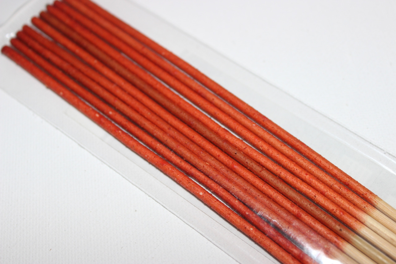 Transparente Kunststoffverpackung mit roten Räucherstäbchen, glatte Oberfläche, naturbelassenes Ende, auf weißer Unterlage.